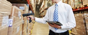 man in tie holding tablet and scanner, scanning boxes in warehouse