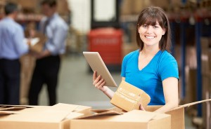 woman in warehouse holding box with tablet in hand