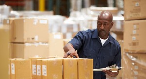 warehouse worker holding clipboard and looking at stack of boxes