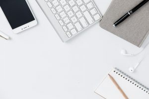 flat lay of desk with keyboard phone, note book and pen