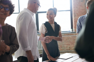 Smiling woman shaking a man's hand in a room of people